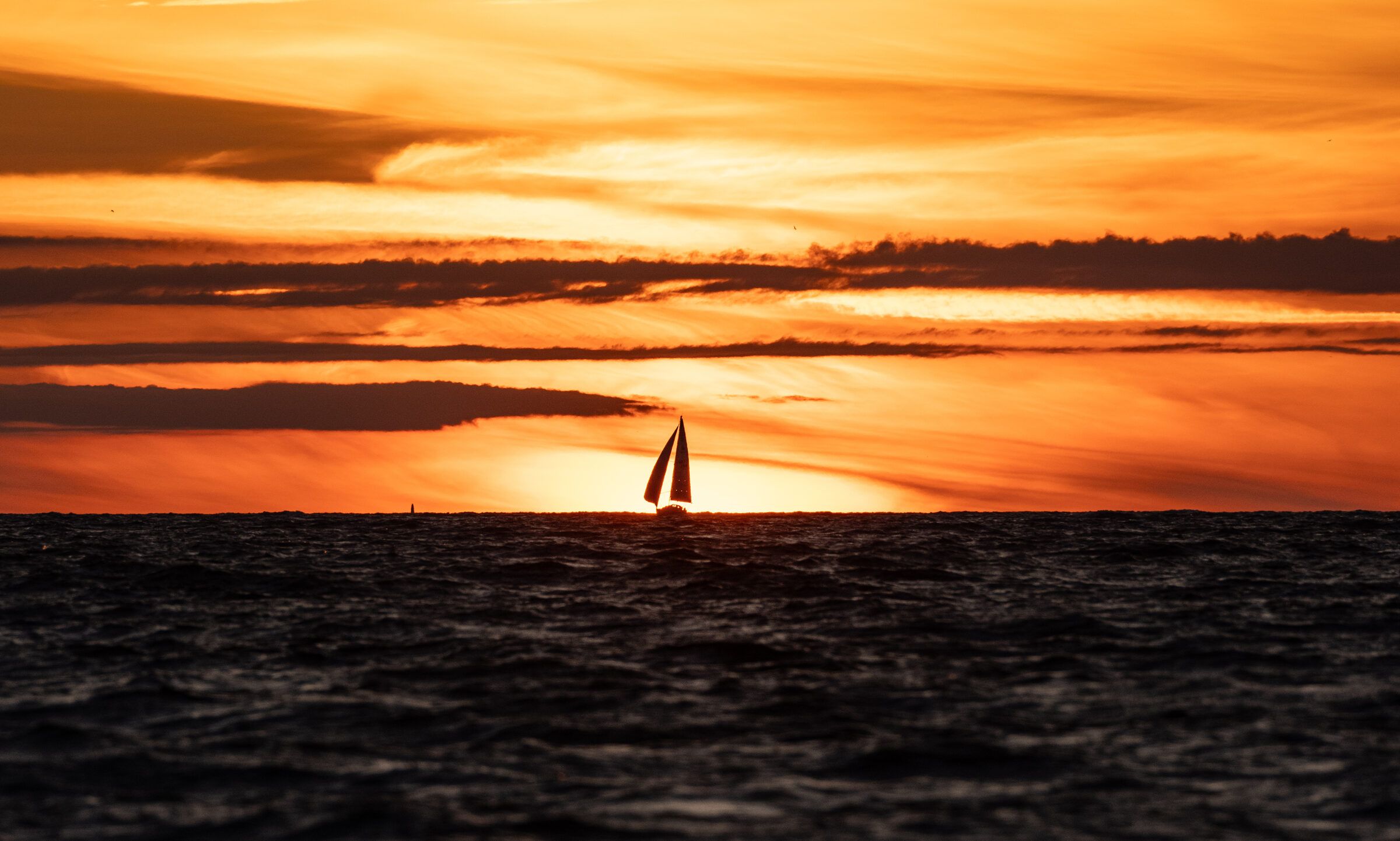 A sailboat on the horizon under a banded orange sunset, dark water below